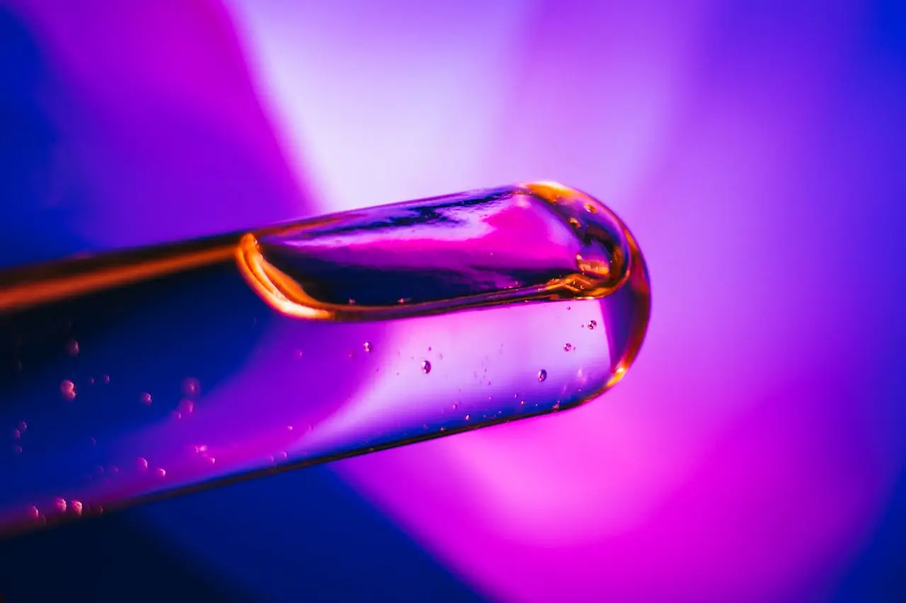 Close-up of an oil dropper with vibrant violet and pink lighting, creating an abstract feel.